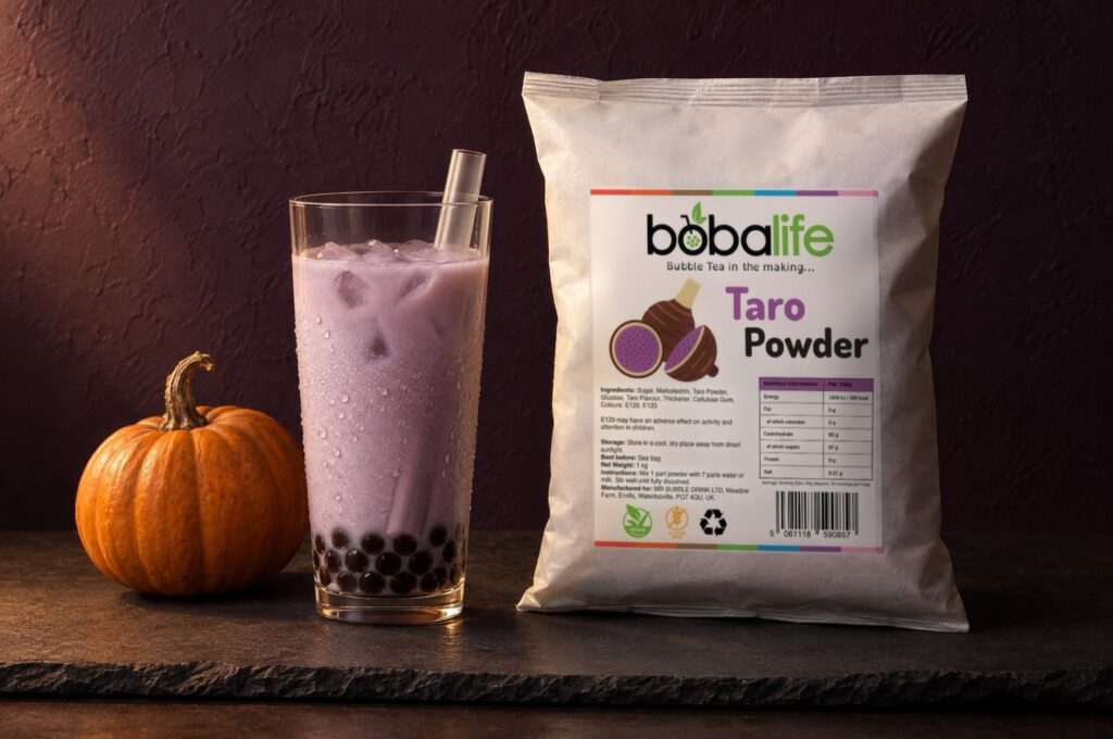 Taro milk tea with black pearls beside a bag of Bobalife taro powder and a small pumpkin