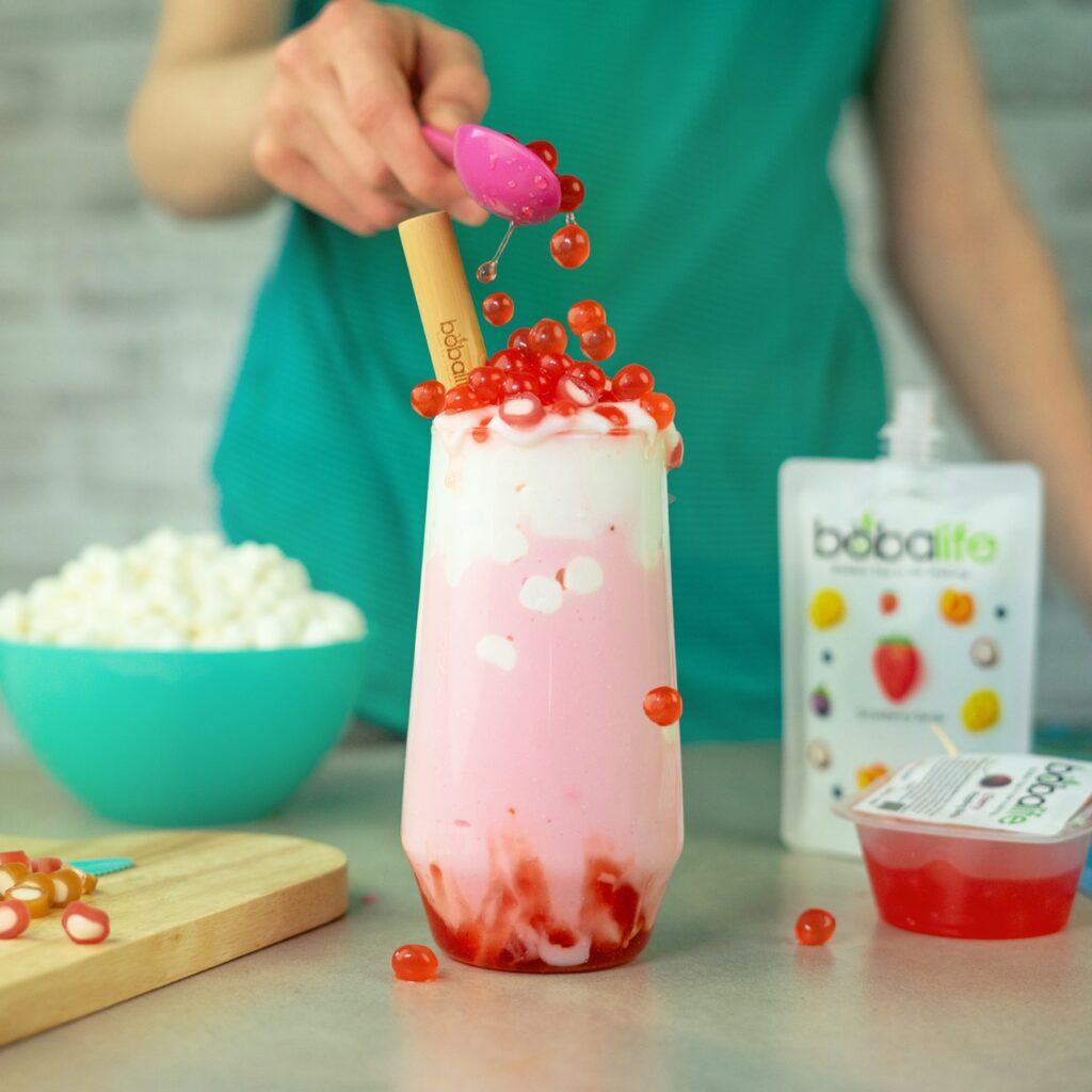 Strawberry popping boba being dropped onto a pink shake