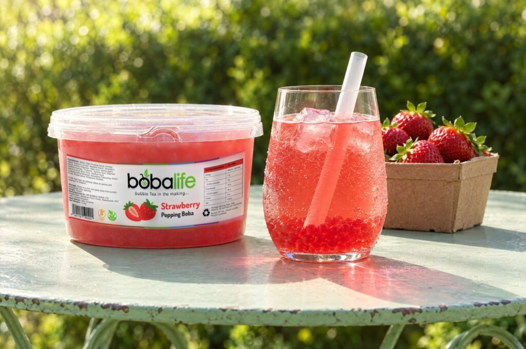 Strawberry iced drink with strawberry popping boba beside a 1.6kg tub on a garden table