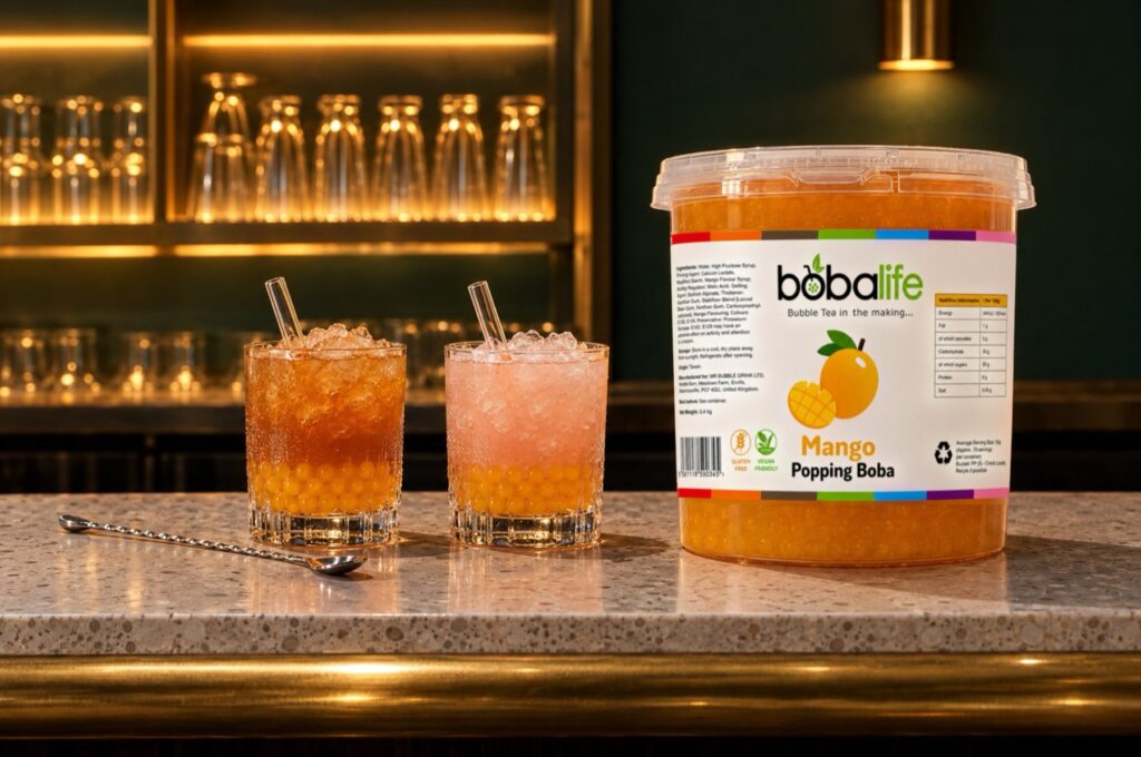 Two cocktails topped with mango popping boba beside a 3.4kg tub on a bar